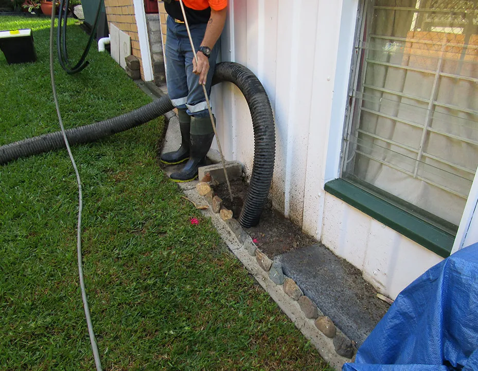 Worker performing vacuum excavation next to house wall